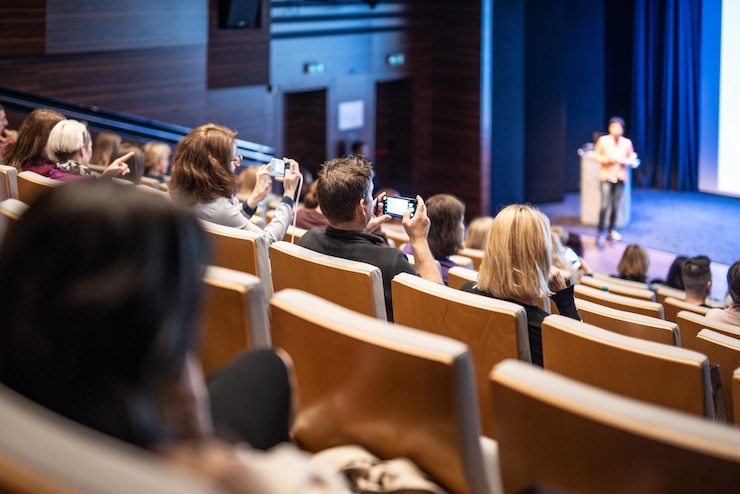 Foto der redner hält einen vortrag im konferenzsaal bei einer geschäftsveranstaltung. hintergrundansicht von unerkennbaren menschen in