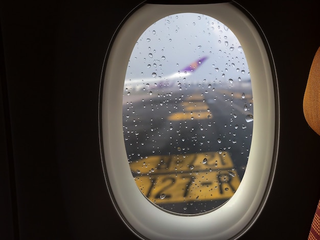 Der Regen fällt auf das Glas außerhalb des Passagierflugzeugfensters, das auf der Landebahn geparkt ist.