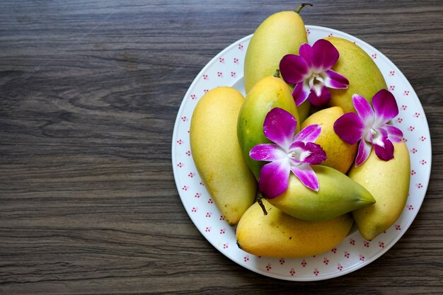 Der reife Mango-Barrakuda mit verzierter Dendrobium-Orchideenblume auf dem Teller auf Holzhintergrund