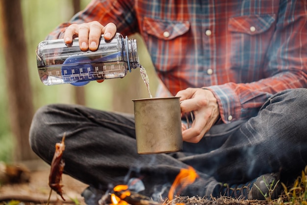 Der Reisende gießt Wasser aus einer Flasche in einen Metallbecher