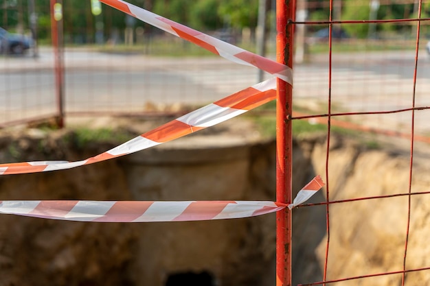 Foto der reparaturort auf der stadtstraße ist mit einem rot-weißen signalband eingezäunt reparaturarbeiten von städtischen versorgungsunternehmen gefahr des sturzes von einer höhe in eine grube