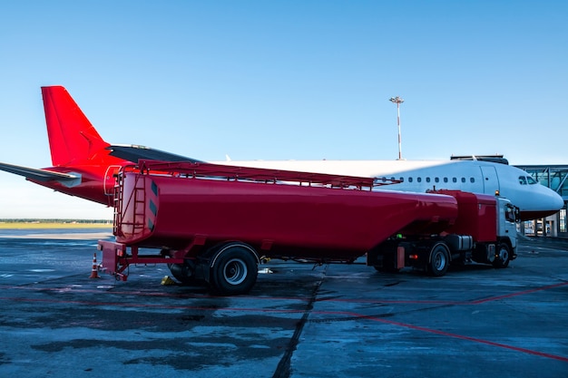 Der rote Tanker betankt das auf einer Fluggastbrücke auf dem Vorfeld des Flughafens geparkte Flugzeug