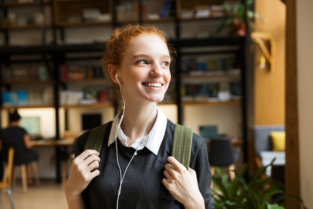 Der rothaarige Student, der drinnen in der Bibliothek posiert, macht Musik mit Kopfhörern