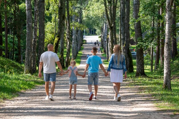 Der Rückblick auf eine Familie auf einem ruhigen Spaziergang ein Vater schwingt die Jüngste hoch, während ihre Geschwister sich die Hände halten neben einem perfekten Symbol der Einheit und sorglosen familiären Momente