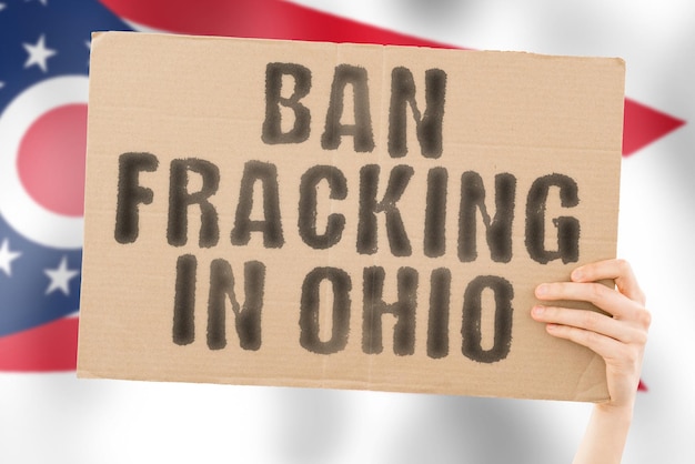 Der Satz Ban Fracking in Ohio auf einem Banner in Männerhand mit verschwommener Ohio-Flagge im Hintergrund Naturextrakt Stop Pipe Energy Drill Raw Power Fuel Fossil Crisis