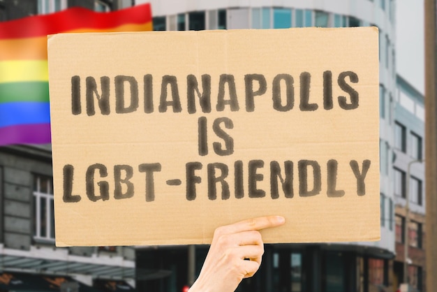 Der Satz "Indianapolis ist LGBT-freundlich" auf einem Banner in Männerhand mit verschwommener LGBT-Flagge im Hintergrund. Menschlichen Beziehungen. unterschiedlich. Vielfältig. Freiheit. Sexualität. Soziale Fragen. Gesellschaft