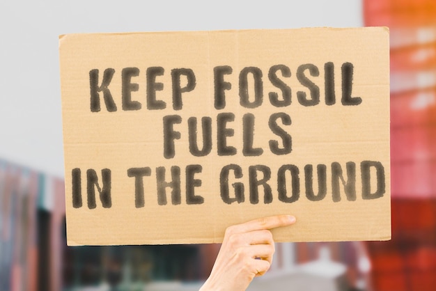 Der Satz Keep Fossil Fuels in the Ground auf einem Banner in Männerhänden mit verschwommenem Hintergrund Carbon Petrol Oil Action Fuel Energy Drilling Refuse Deny Justice Change Refusal Reject