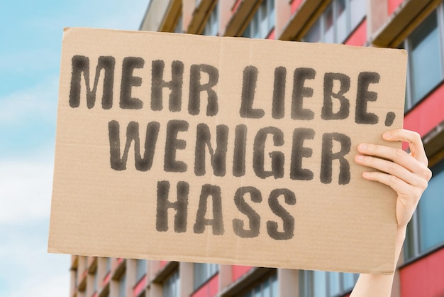 Der Satz Mehr Liebe weniger Hass steht auf einem Banner in den Händen der Männer mit verschwommenem Hintergrund Hoffnung Heilung Sanftheit Einheit Inklusion Vielfalt Gleichheit Respekt Akzeptanz Toleranz Vergebung