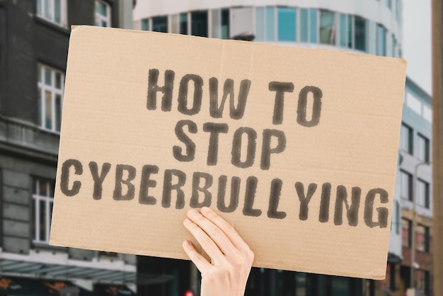 Der Satz "Wie man Cybermobbing stoppt" auf einem Banner in der Hand von Männern mit unscharfem Hintergrund. Grausam. Verhalten. Verhütung. Verängstigt. Das Bewusstsein. Cyber-Belästigung. Digitale Sicherheit. Verzweifeln. Kontrolle