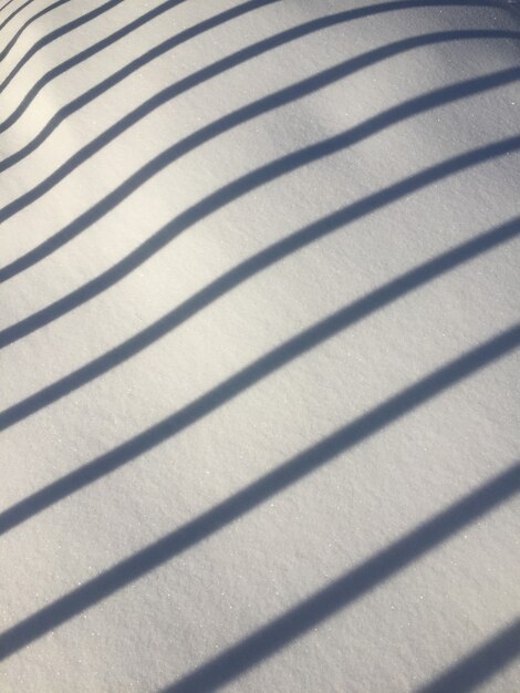 Der Schatten des Zauns auf dem Schnee an einem sonnigen Tag. diagonale parallele Schattenlinien auf Weiß