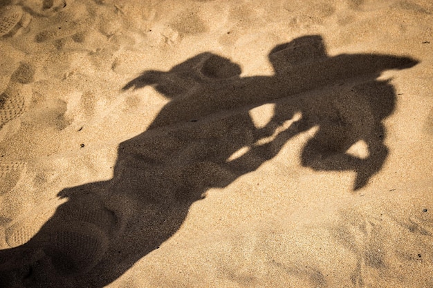 Der Schatten einer Person, die ein Kind am Strand in der Luft hält, aufgenommen an einem sonnigen Tag