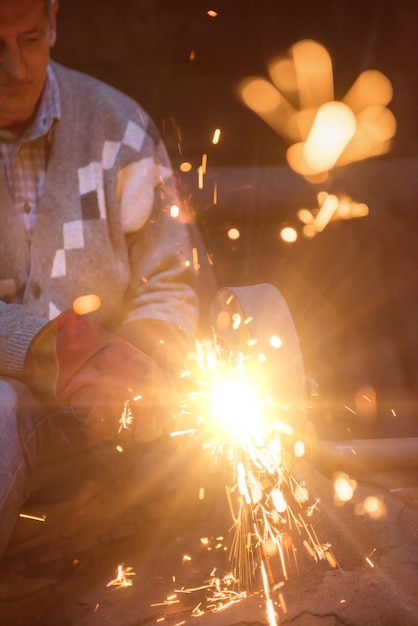 der Schmied, der in seiner traditionellen Werkstatt Metallprodukte poliert, während er mit einer Schleifmaschine Funken erzeugt