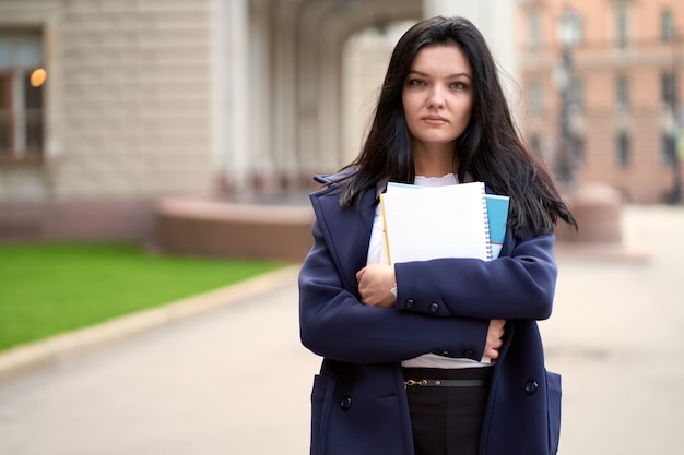 Der schöne ernste intelligente Mädchen Brunettestudent, der Notizbücher und Lehrbücher hält, steht an der Universität