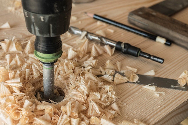 Der Schreiner bohrt mit einem Bohrer ein Werkstück aus Holz. Ein Bohrer, ein Stift und eine Ecke