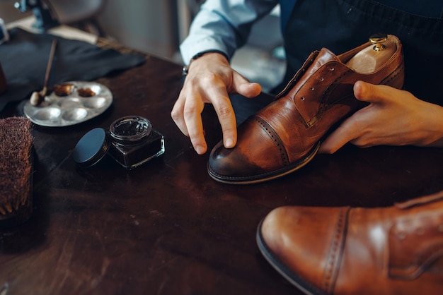 Der Schuhmacher wendet einen schwarzen Schuhcreme- und Schuhreparaturservice an. Handwerkskunst, Schuhmacherwerkstatt, Meisterarbeiten mit Stiefeln, Schusterladen