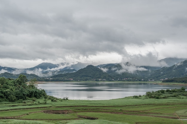 Der See spiegelt die grünen Berge, die neblig sind