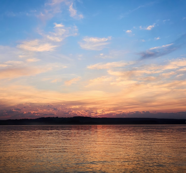 Der Sonnenuntergangshimmel spiegelt sich im Wasser vor dem Hintergrund eines fernen dunklen Ufers