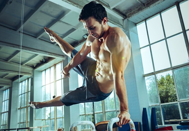 Der Sportler, der schwierige Gymnastikübungen im Fitnessstudio durchführt. Sport, Bewegung, Turner, Gesundheit, Training, Sportlerkonzept. Modell mit kaukasischer Passform