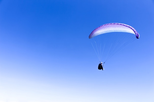 Der Sportler fliegt auf einem Gleitschirm in den blauen Himmel