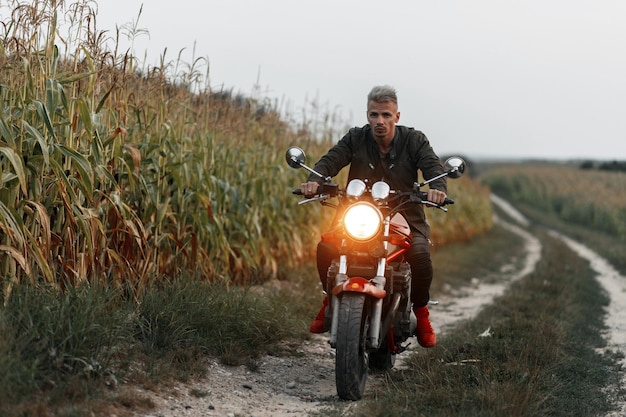 Der stilvolle schöne Hipster-Mann in der Militärjacke fährt ein Motorrad mit Licht im Feld