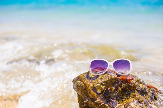 Der Strand mit Sonnenbrille und Sandale auf dem Felsen, Kopienraum für Text. Konzept des Sommers.