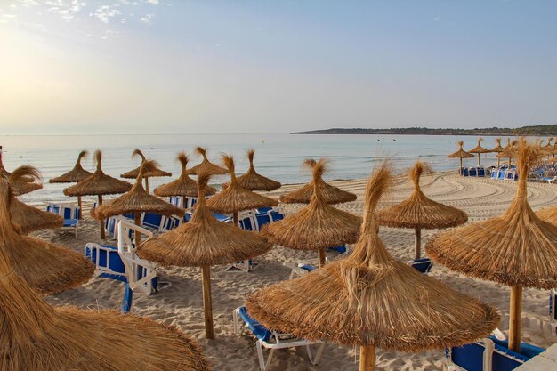 Der Strand von Cala Millor, der von Regenschirmen und Klappstühlen bedeckt ist und vom Meer umgeben ist, auf Mallorca, Spanien