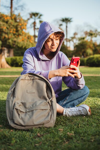 Der Student benutzt ein Mobiltelefon im Park. Sie trägt einen lila Hoodie.