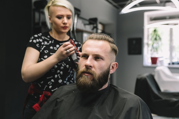 Der stylist hält den schnurrbart des brutalen bärtigen mannes im friseursalon.