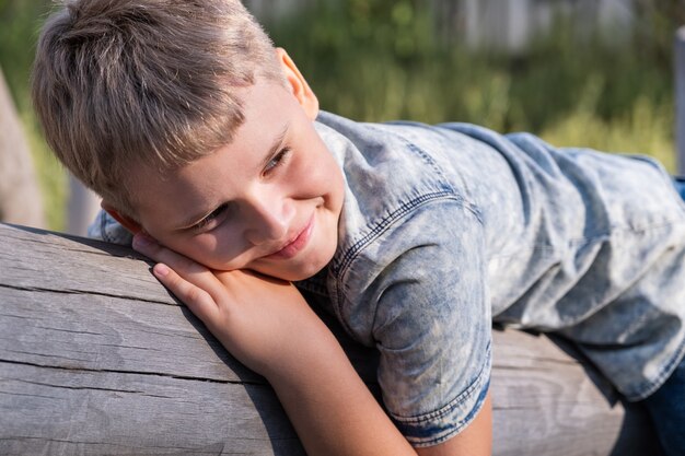 Der süße blonde Junge liegt auf einem Holzbalken auf dem Spielplatz in einem öffentlichen Park.