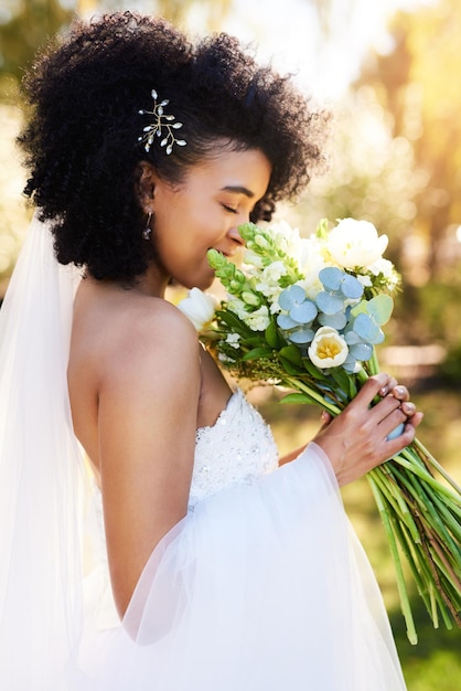 Der süße Geruch von Liebe und Glück Aufnahme einer glücklichen und schönen jungen Braut, die an ihrem Hochzeitstag im Freien an ihrem Blumenstrauß riecht