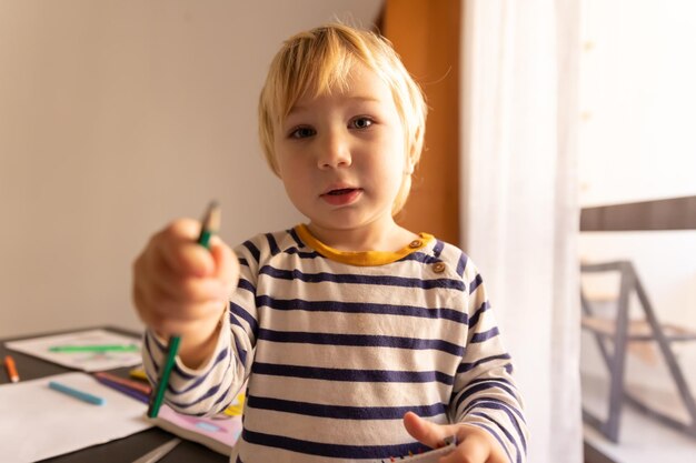 Der süße kleine blonde Junge hält einen Buntstift in die Höhe