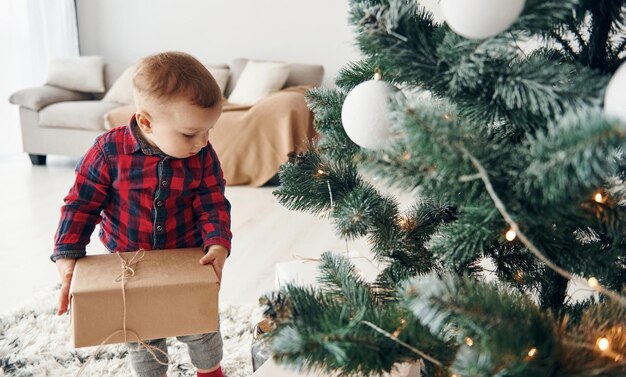 Der süße kleine Junge in festlicher Kleidung ist zur Neujahrszeit drinnen in der Nähe des Weihnachtsbaums