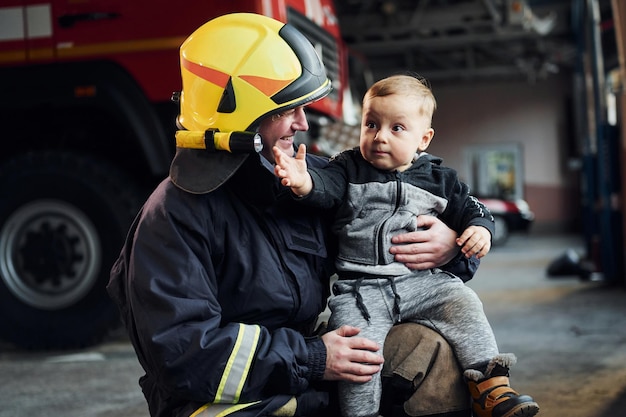 Der süße kleine Junge ist mit einem männlichen Feuerwehrmann in Schutzuniform