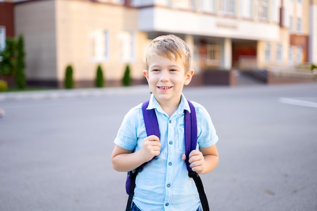 Der süße kleine Junge mit Rucksack steht in der Nähe der Grundschulkindererziehung auf dem Schulhof