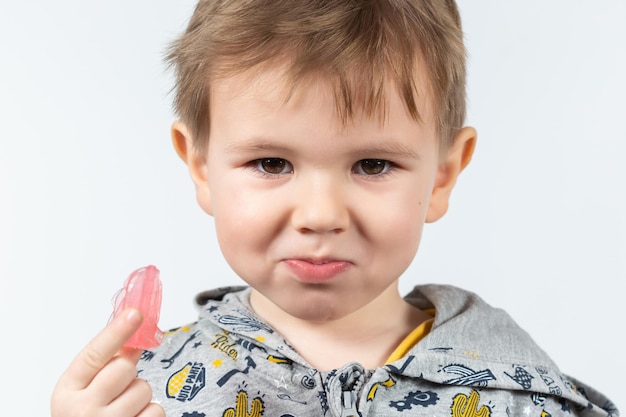 Der süße kleine kaukasische Junge mit blonden Haaren hält einen rosafarbenen myofunktionellen Zahntrainer auf weißem Hintergrund. dental tariner wurde entwickelt, um die wachsenden Zähne auszugleichen und den Biss zu korrigieren