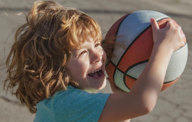 Der süße, lächelnde, aufgeregte Junge spielt Basketball, lustiges Kindergesicht, Nahaufnahme