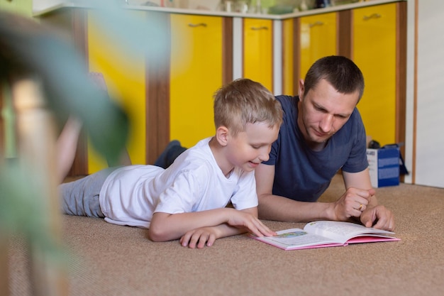 Der süße Sohn liest dem auf dem Boden liegenden Vater ein Buch vor