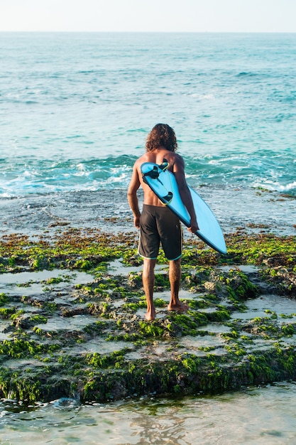 Der Surfer hält ein Surfbrett am Ufer des Indischen Ozeans