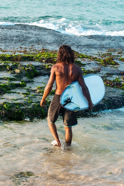 Der Surfer hält ein Surfbrett am Ufer des Indischen Ozeans