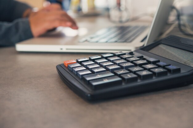 Der taschenrechner wird mit einem laptop auf einen bürotisch gestellt und das team arbeitet hinter den kulissen.