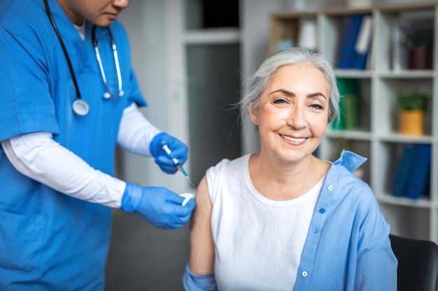 Der tausendjährige Arzt spritzt einer lächelnden älteren Patientin im Inneren der Klinik eine Injektion