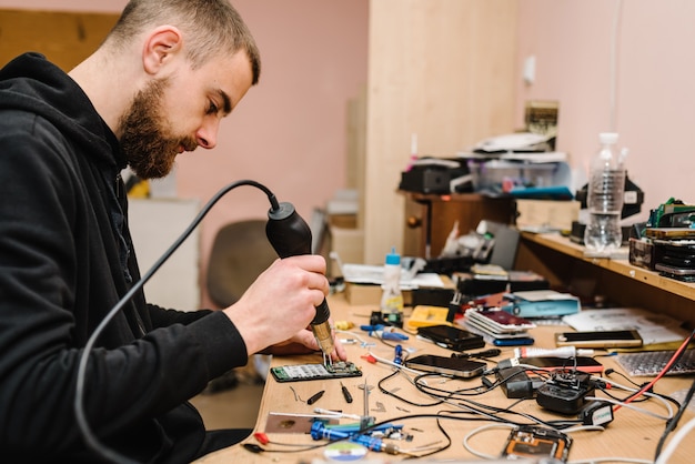 Foto der techniker repariert das smartphone-motherboard im labor. konzept von computerhardware, mobiltelefon, elektronik, reparatur, upgrade, technologie. mann, der den prozess der telefonreparatur in der werkstatt zeigt.