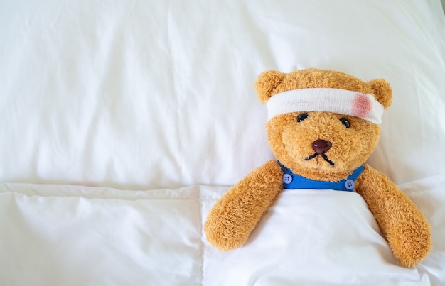 Der Teddybär lag krank im Bett, nachdem er bei einem Unfall verletzt worden war. Lebensversicherung und Unfallversicherung Konzept bekommen