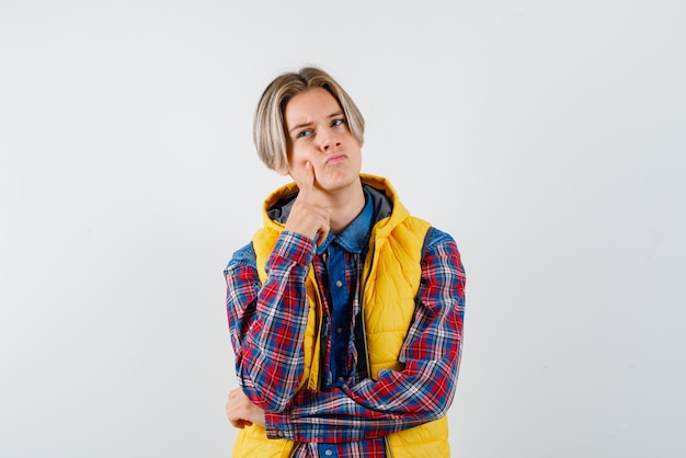 Foto der teenager denkt, indem er seinen rechten zeigefinger auf weißem hintergrund an die wange hält