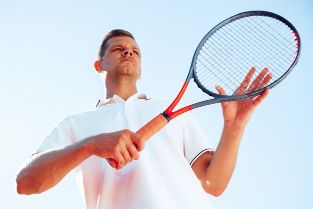 Der Tennisspieler eines jungen Mannes überprüft seinen Schläger, um ein Spiel zu starten