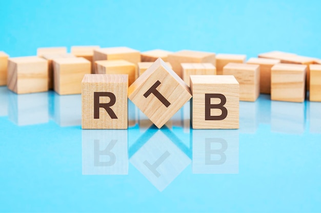 Der Text RTB Real Time Bidding, der in schwarzen Buchstaben auf den Holzwürfeln geschrieben ist, befindet sich auf einem hellblauen Glasoberflächenkonzept, das Wort bildet, mit Würfeln im Hintergrund