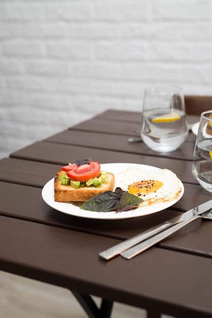 Der Tisch mit Frühstück mit Sandwiches und Spiegeleiern mit Wasser mit Zitrone