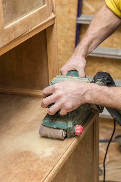 Der Tischler restauriert das alte Holz-Sideboard mit einer elektrischen Schleifmaschine.