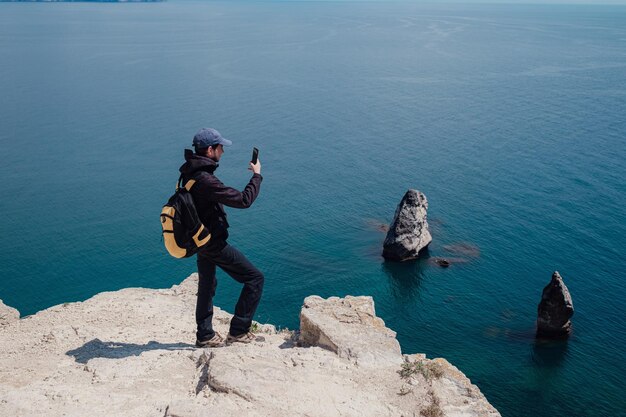 Der Tourist macht auf dem Smartphone ein Foto von einer unglaublich malerischen Aussicht von einer Klippe auf dem Meer