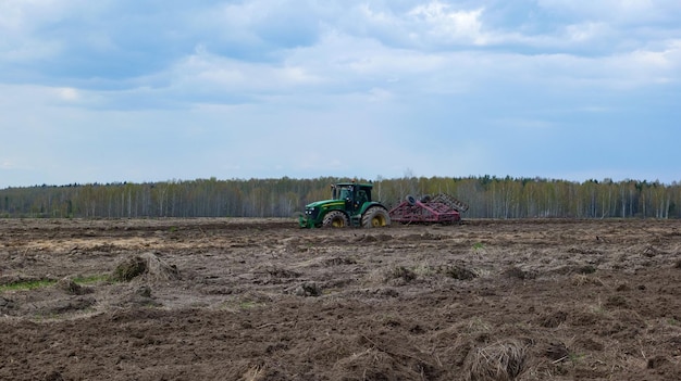 Der Traktor bewirtschaftet das Land auf einem Feld in der Nähe des Waldes